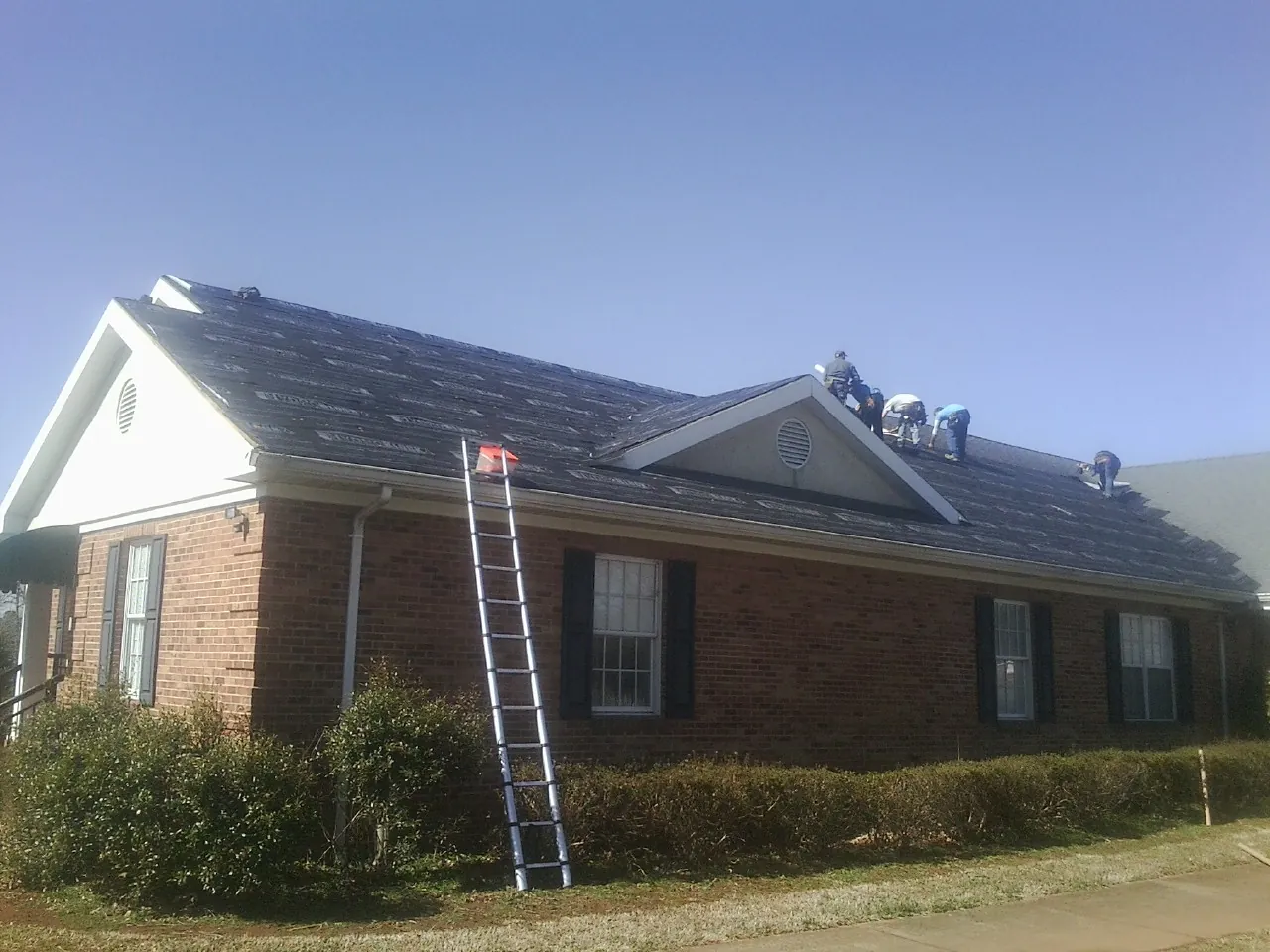 Crew tearing shingles off a brick ranch roof with a ladder set — Metal Roof Repair work by our crew in Greene