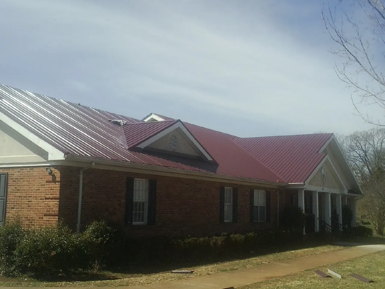 Red metal roof with gabled entries on a long brick building, from a Hail Damage Roof Repair job in Greene