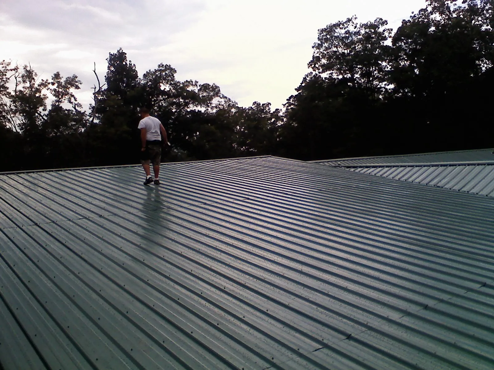 Roofer walking a wide expanse of new green metal roofing in Greene
