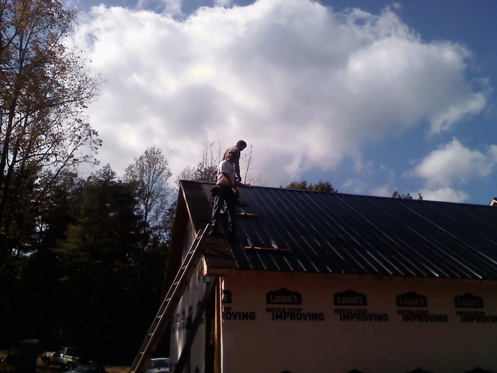 Roofer fastening dark metal panels high against a cloudy sky, from a Roof Inspection job in Greene