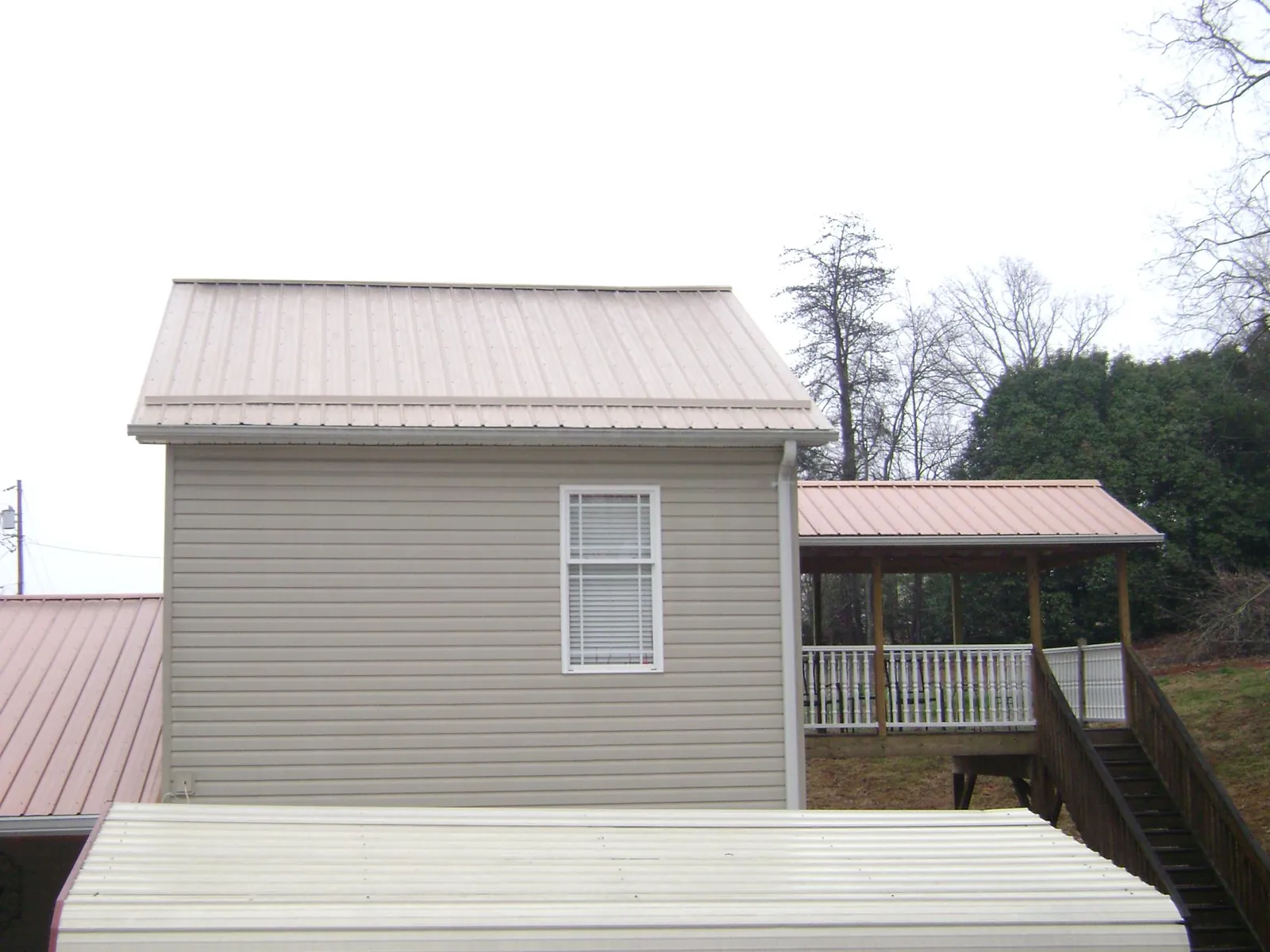 Tan metal roofs on a two story addition and attached porch, from a Roof Replacement job in Greene